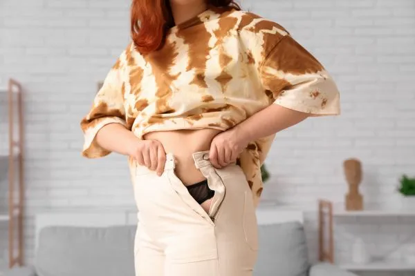 Image of woman trying to do her trousers up after pregnancy weight gain Craigmillar