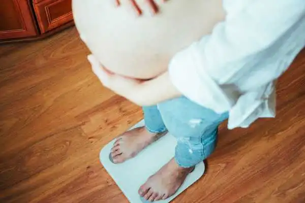 Image of woman weighing herself and experiencing weight gain through pregnancy Craigmillar